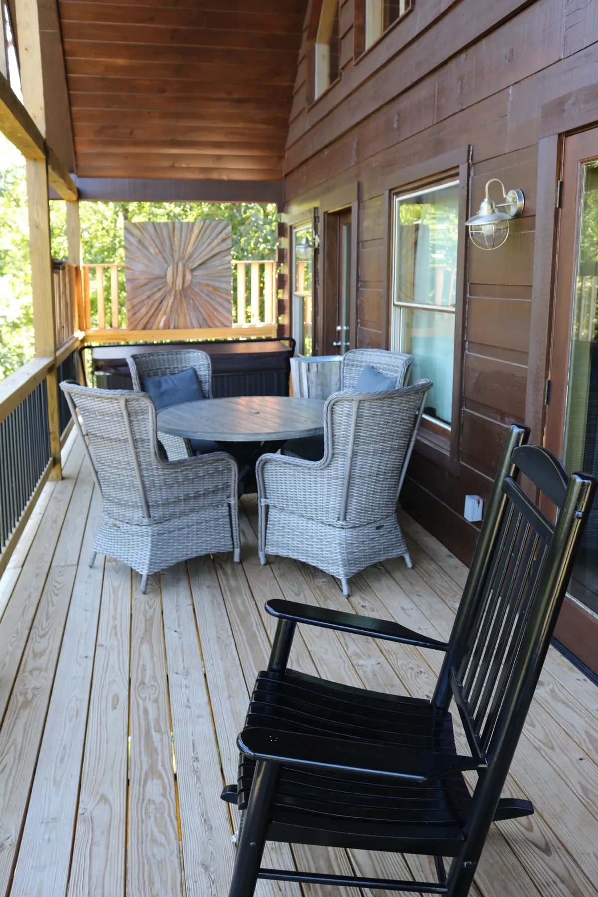 This exterior image showcases wicker chairs and a circular table set against a rustic wooden wall, perfect for sipping morning coffee or enjoying a quiet moment. The setup, with its inviting furniture and natural light, echoes relaxation and the versatile use of the deck space.