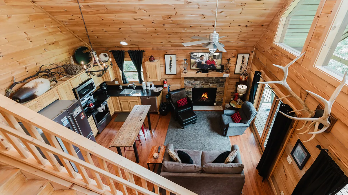 This image features a kitchen island, a dining table, large windows with natural views, and a cozy fireplace. The open-plan arrangement encourages group gatherings, and the combination of cooking and dining spaces creates an inviting environment.