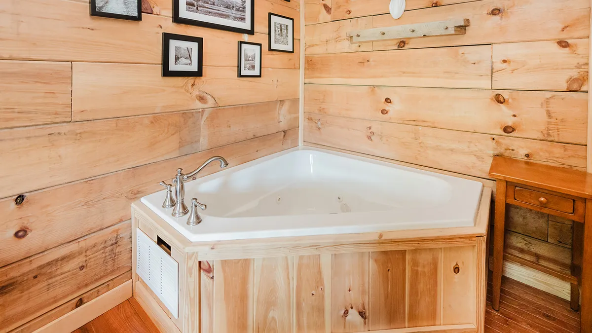 A tranquil indoor space showcasing a Jacuzzi tub set against wooden paneling, with framed photographs and a small wooden side table nearby. The tub invites indulgent soaks, and the setting is quiet and restful.