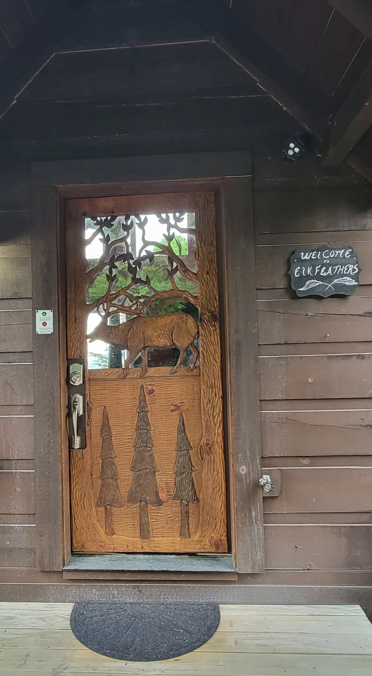 This image features the rustic wooden front door of Elk Feathers, complete with intricate carvings and a welcoming sign. The natural wood textures and inviting entryway set the tone for a cozy cabin experience, hinting at the adventures and gatherings that await inside.