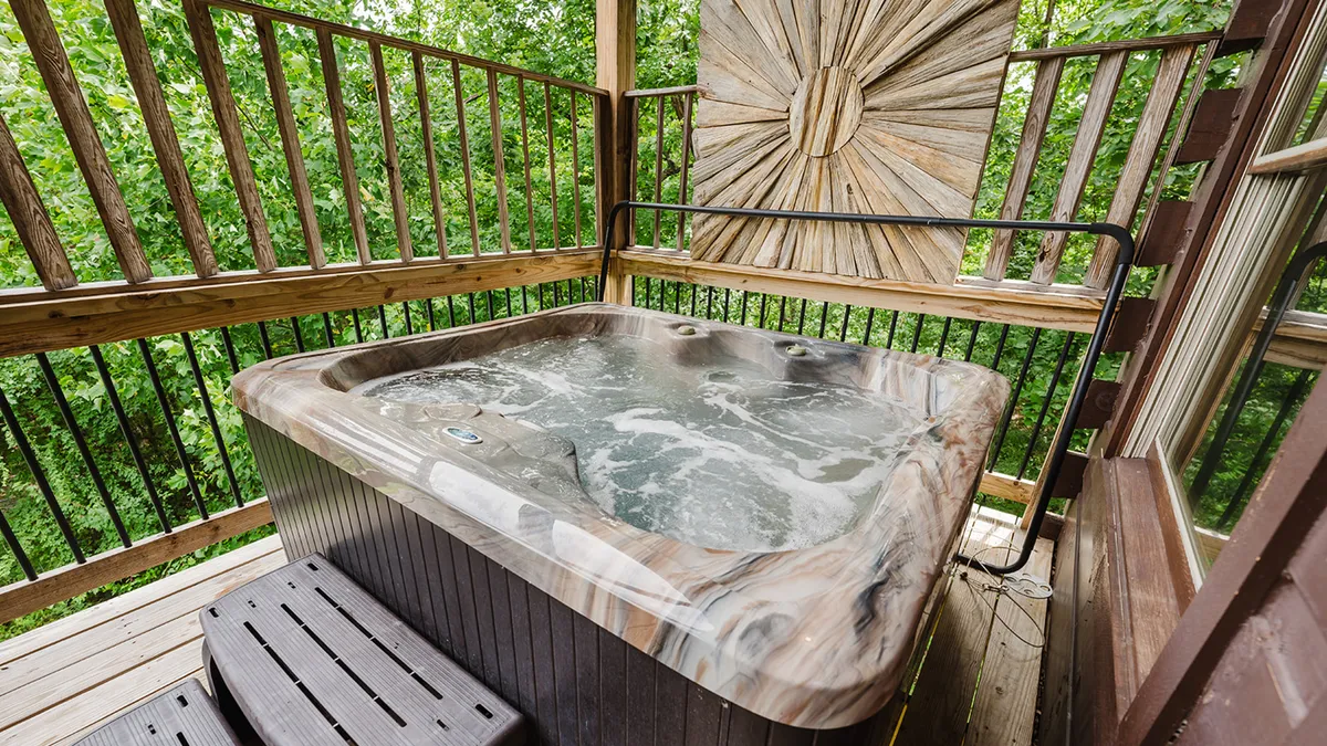 This interior image features a private hot tub with wooden railing and a decorative wall feature, offering views of the surrounding natural landscape. The tranquil mood suggests a soothing place to unwind after a day out.